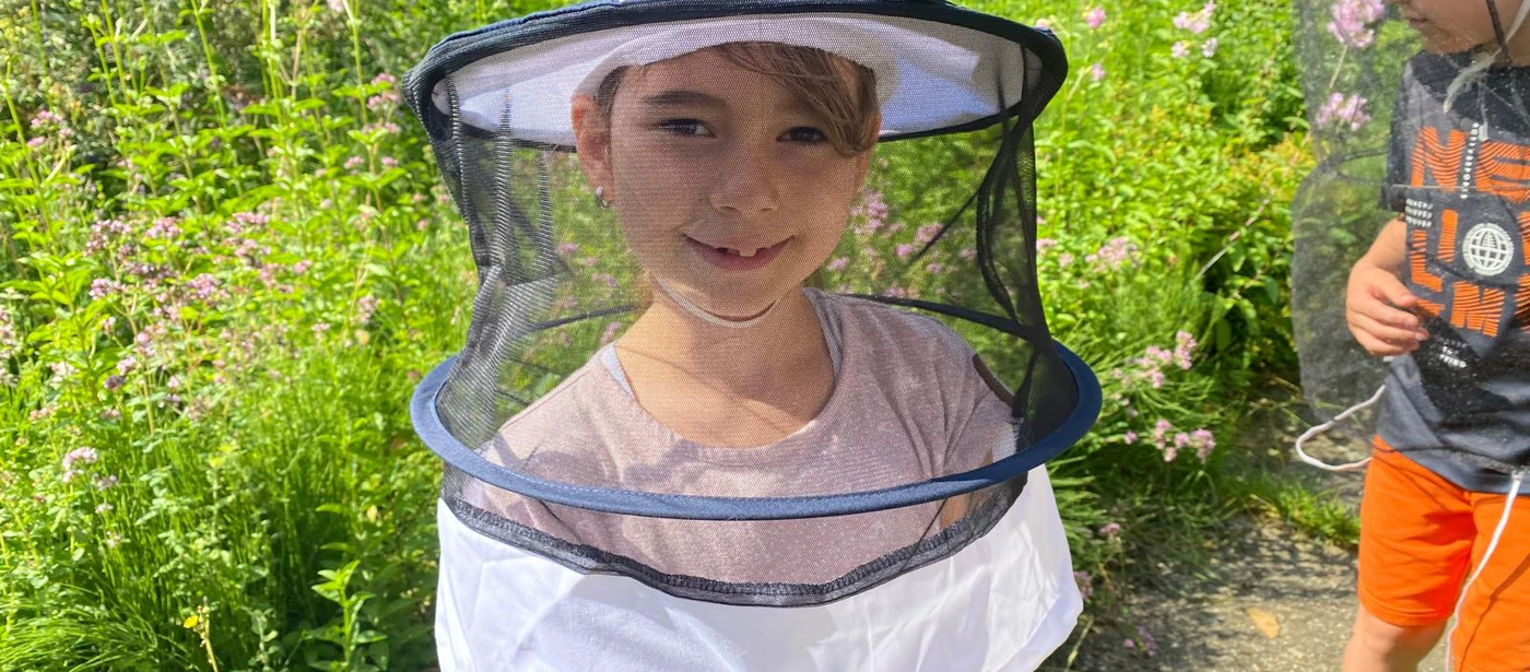 Ein Kind mit Imkerhut im blühenden Garten